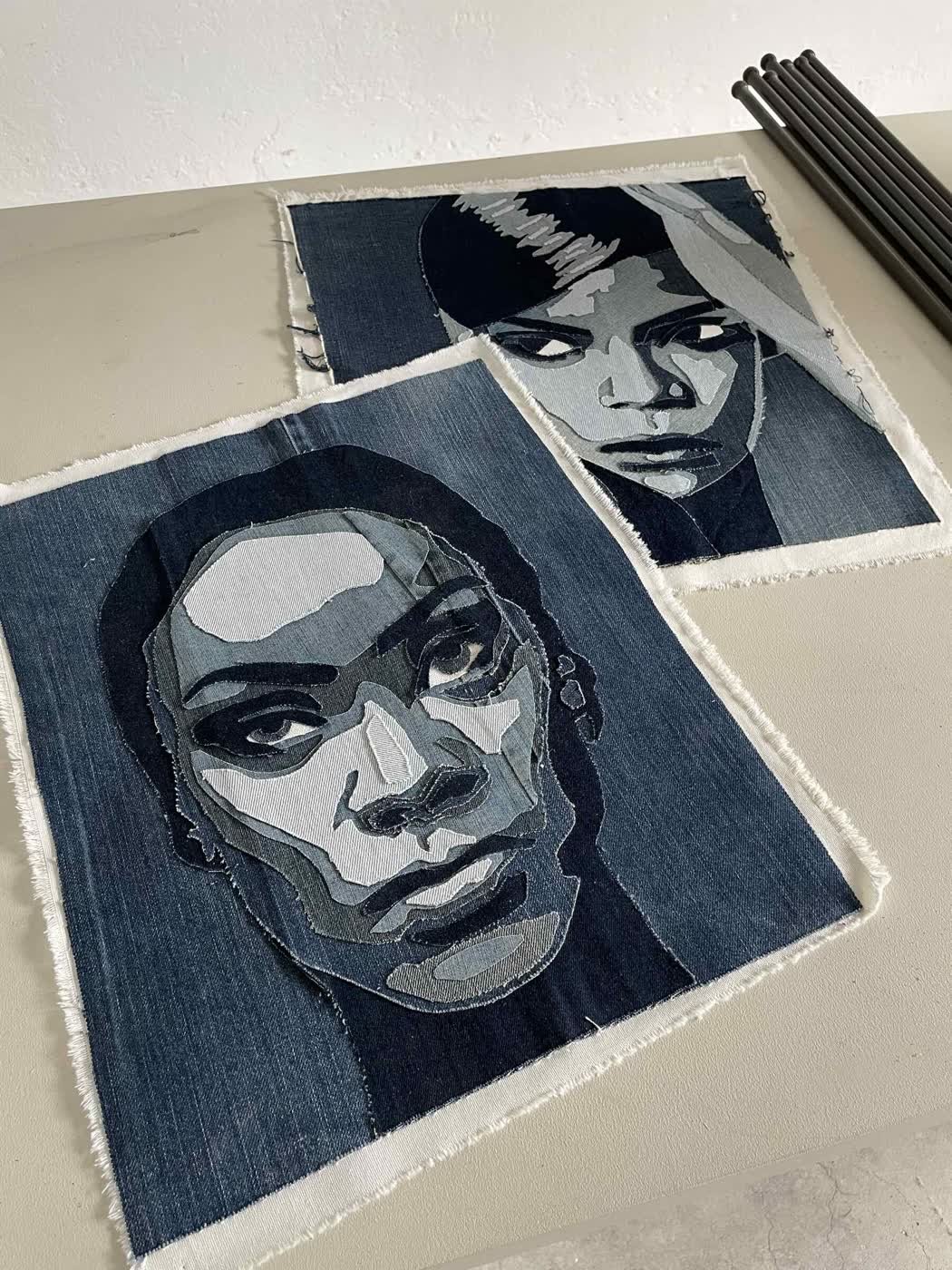 Two portrait faces crafted from layered cut denim, mounted on a beige studio wall.