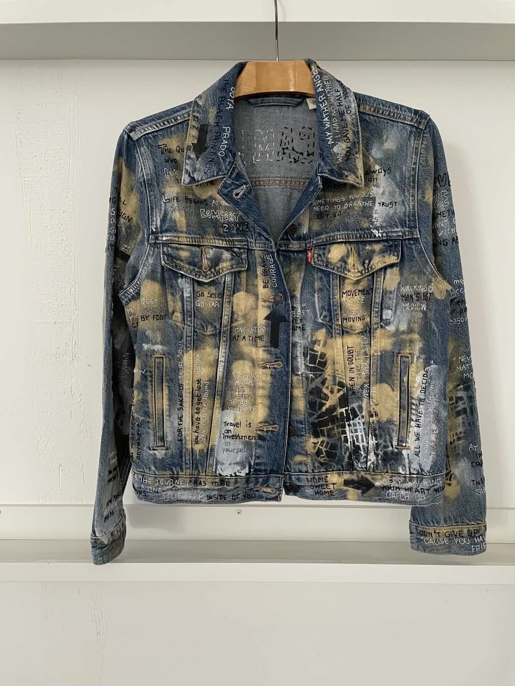 A hand-painted Levi's denim jacket covered in inspirational phrases over a bleached blue-and-tan finish.