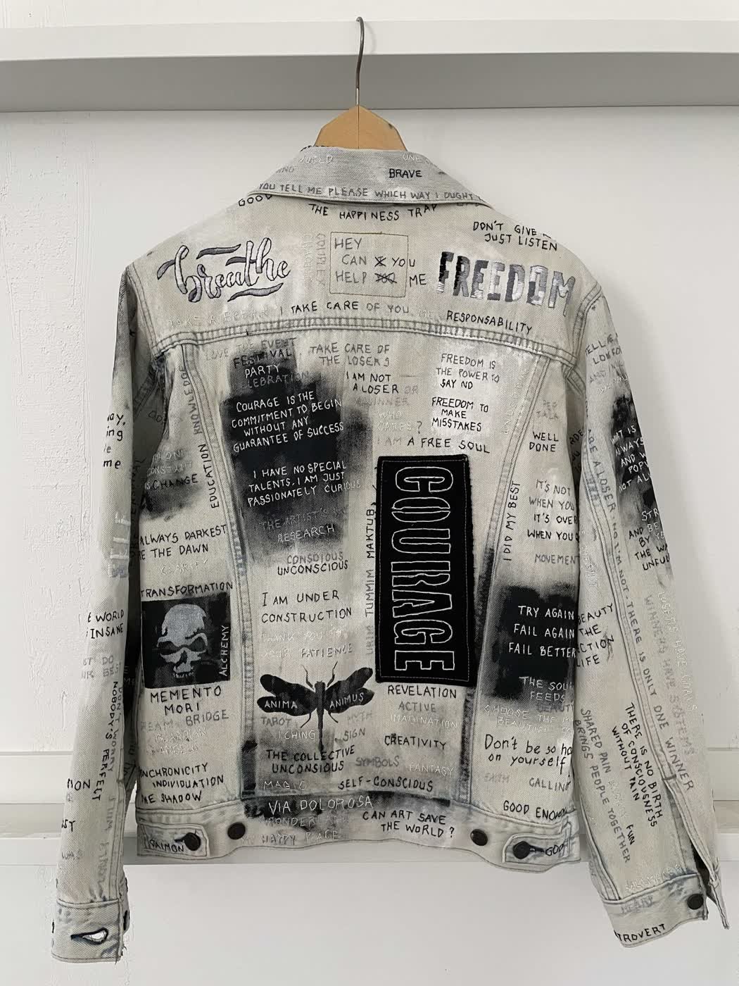 Back of a bleached denim jacket covered in slogans including "Courage", "Freedom" and "Breathe".