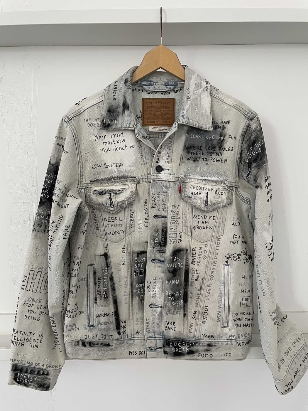 Front of a light-wash Levi's jacket hand-lettered with slogans such as "Rebel at heart" and "Just do it".