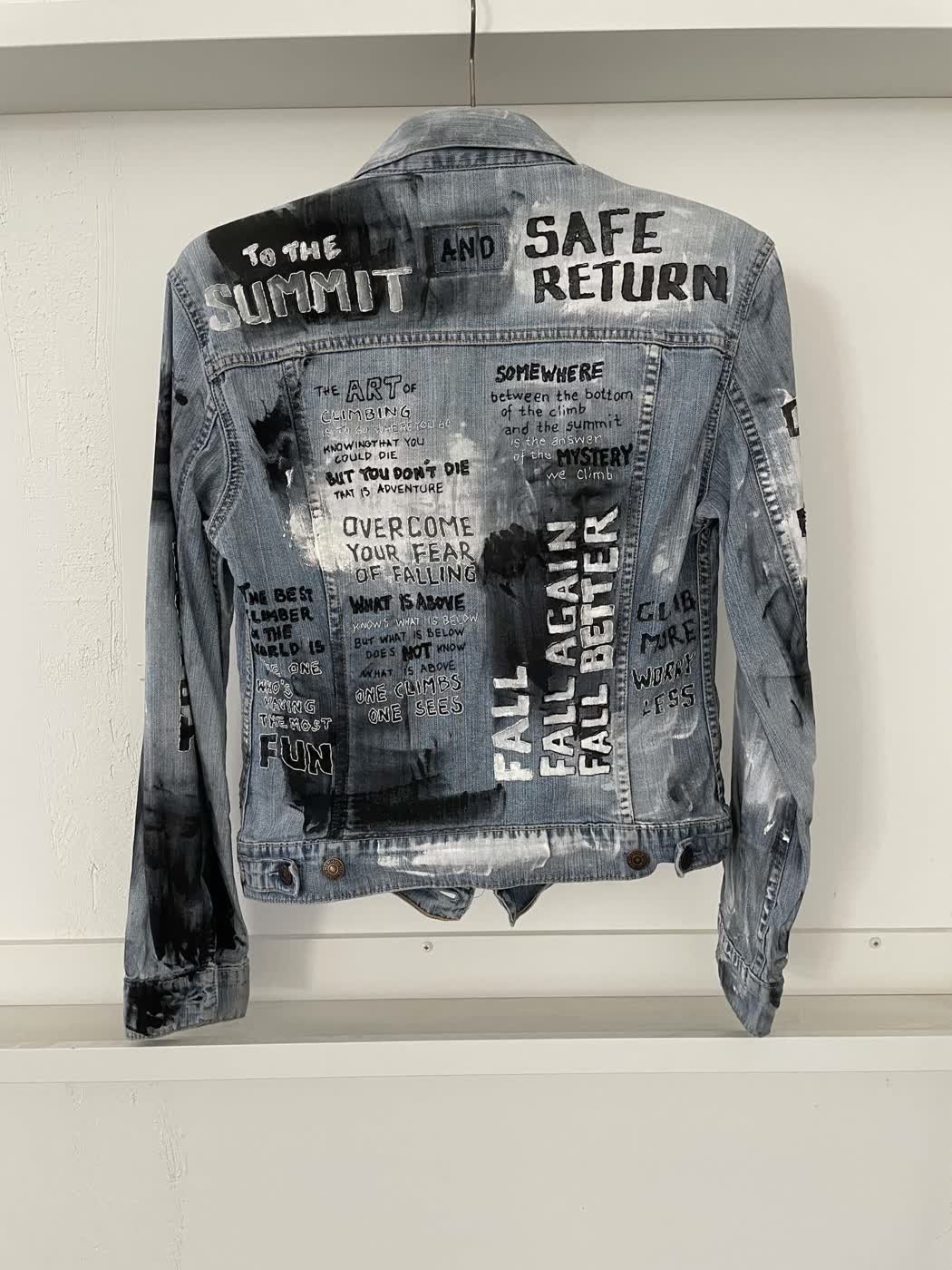 A hand-painted denim jacket with bold climbing slogans including "To the Summit".
