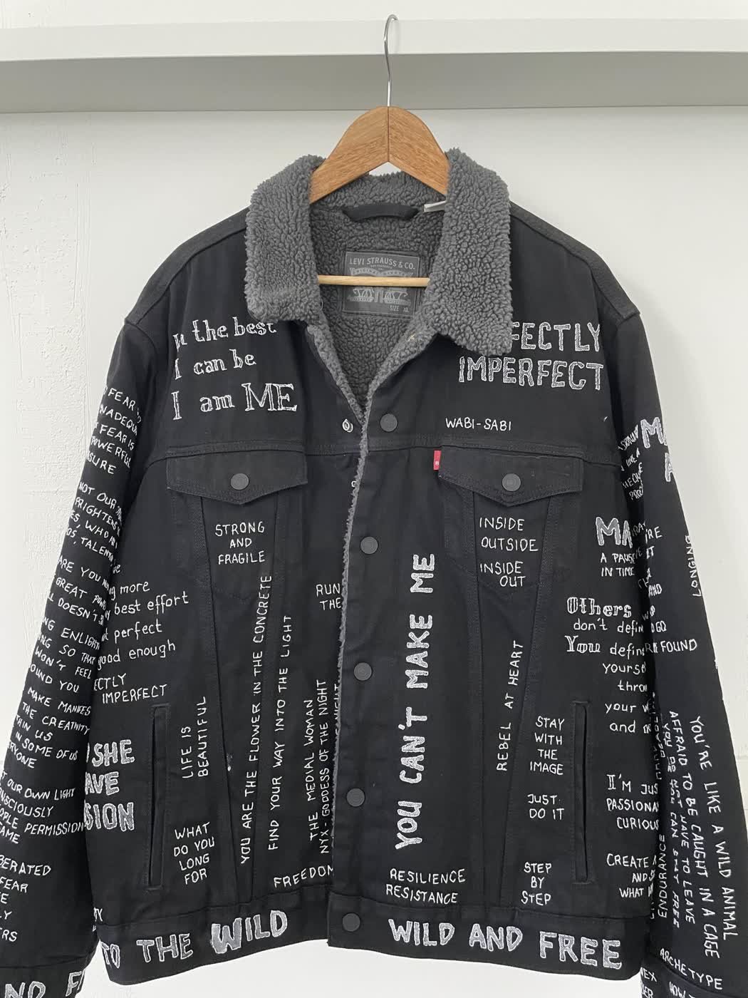 Front of a black Levi's denim jacket painted with slogans such as "Wild and free" and "Perfectly imperfect".