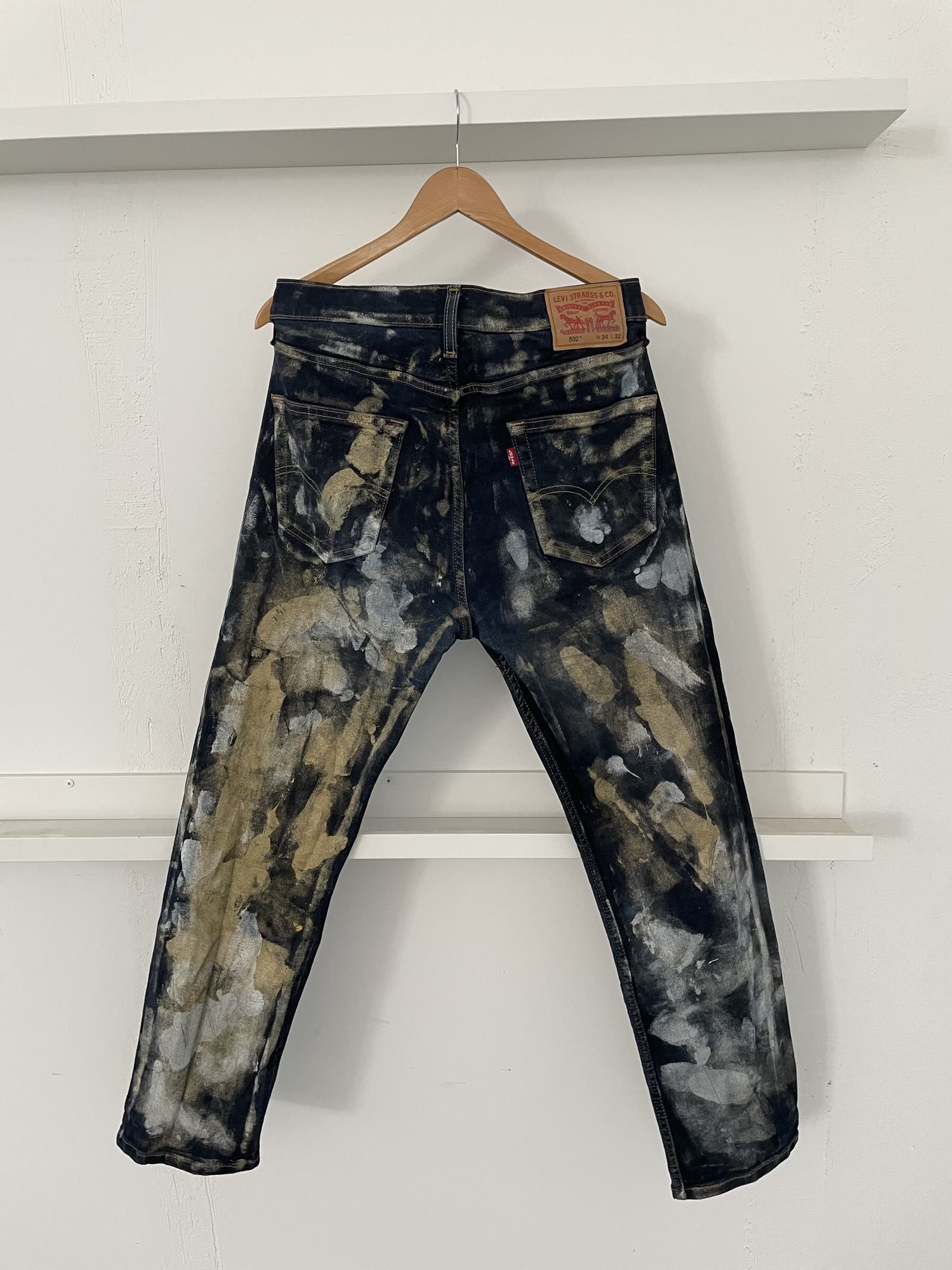 Levi's 502 jeans hand-dyed with a mottled black, olive and silver bleach pattern.