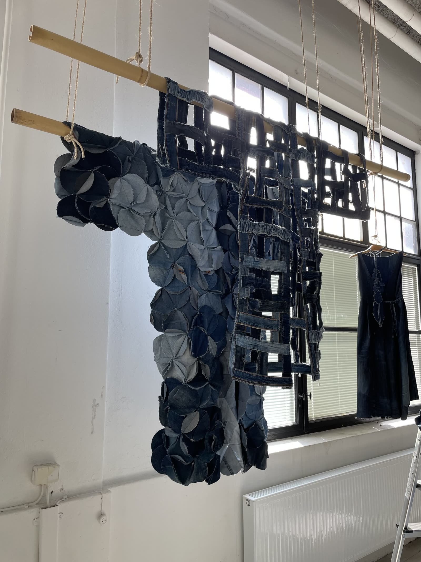 A large tapestry of upcycled jeans suspended from bamboo poles in a bright studio.