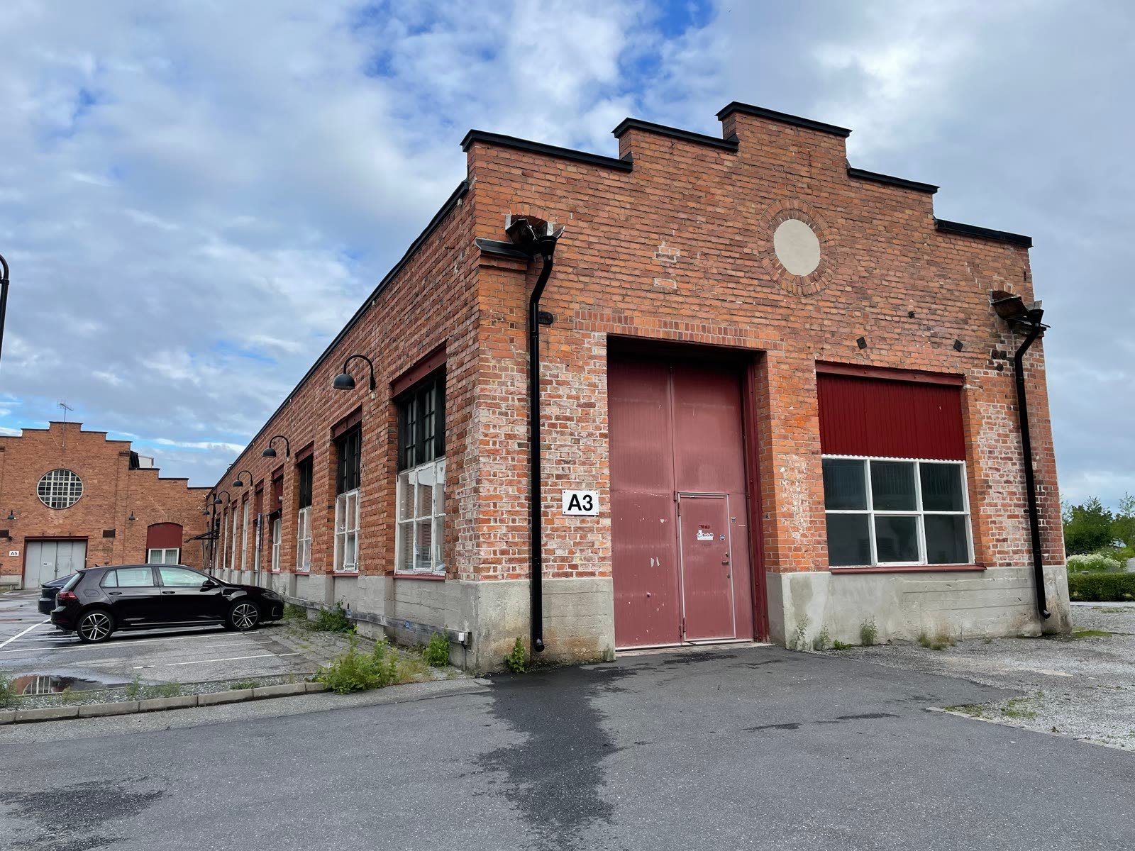 The red-brick industrial building that houses the workshop, seen across the yard, with maroon loading doors.